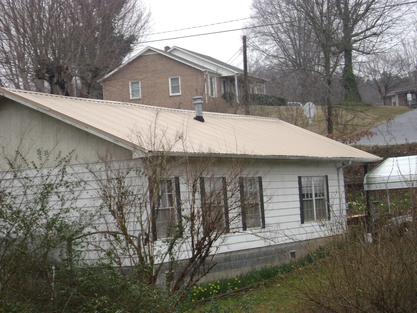Tan metal roof on a white sided house set into a hillside — Commercial Roofing by Roofing Brothers in Linville