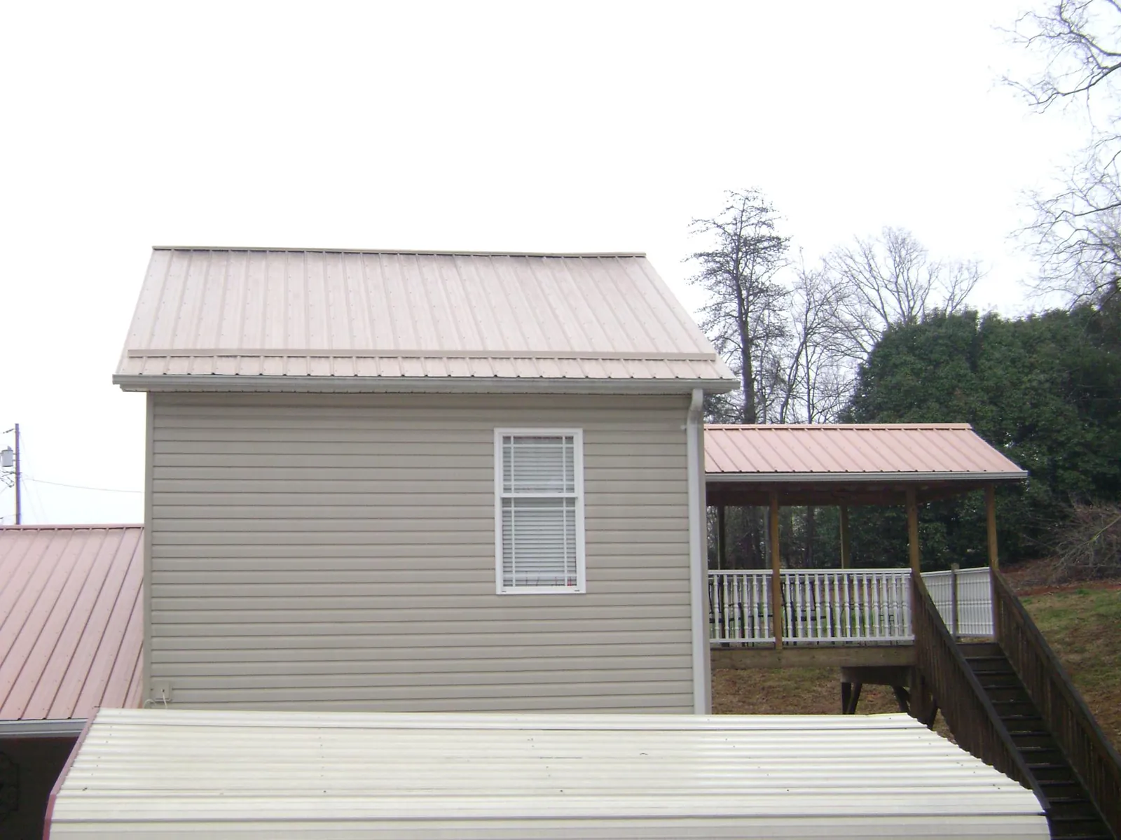 Tan metal roofs on a two story addition and attached porch, from a Roof Replacement job in Linville